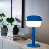 En BLÅSVERK blå bordslampa på hyllan, modern, rundad, vit skärm, mindre än böcker och växter.