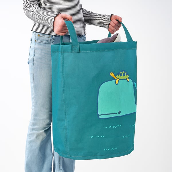 Person som håller en turkos tygväska med grön valdesign och bär den i handtagen.