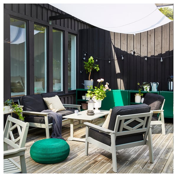 Modern uteplats med svarta fåtöljer, soffa, träbord, grön ottoman, växter och ljusslingor på ett trädäck.