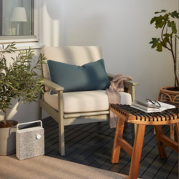 Modern uteplats med stolen BONDHOLMEN beige, blå kudde, växter, träbord och högtalare.