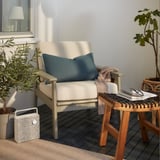 Modern uteplats med stolen BONDHOLMEN beige, blå kudde, växter, träbord och högtalare.