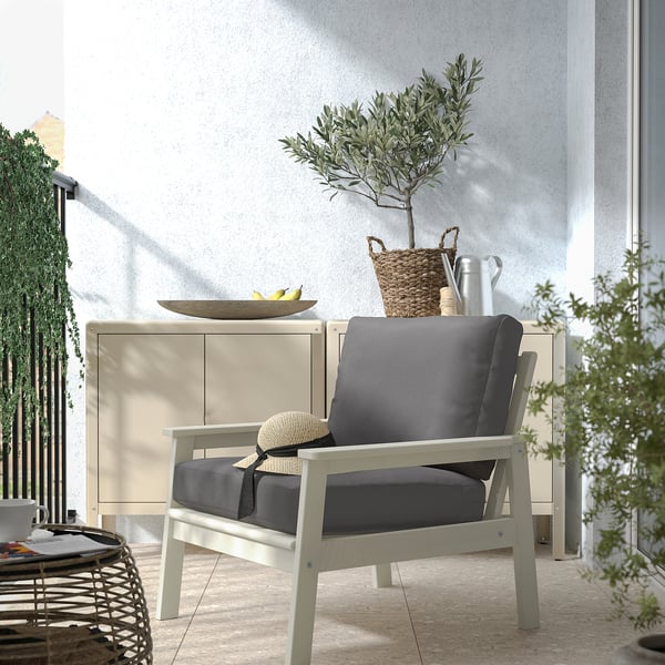 Modern utomhuslounge med BONDHOLMEN grå stoppad stol, vitt skåp och grön växt.