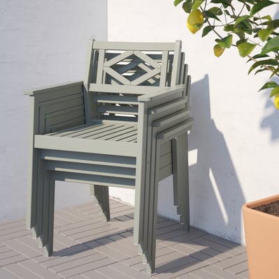 Staplade ljusgrå utomhusstolar i eukalyptus med armstöd och geometrisk ryggdesign mot en ljus vägg.