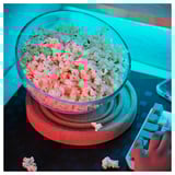 En stor skål med popcorn står på ett smart underlägg, vilket minskar risken för spill. En hand håller en leksak i lego-stil bredvid den.