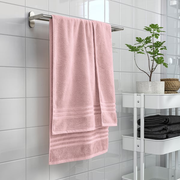 Ljusrosa BROKGLIM handduk hänger bredvid svarta handdukar på hyllan.
