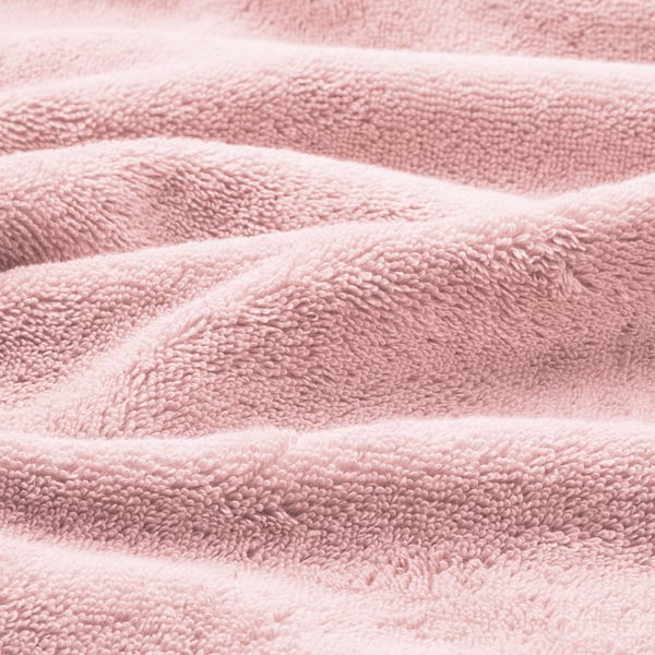 Närbild av mjuka, plyschrosa handdukar i ekologisk bomull med elegant vävd kant, som visar upp hög kvalitet och textur.