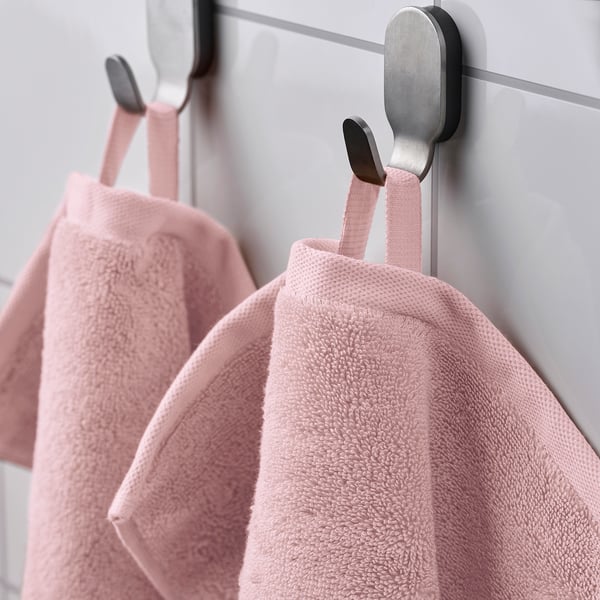 Två rosa handdukar hänger på silverkrokar på en grå vägg.