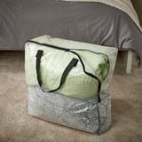 Genomskinlig plastpåse med handtag, vilar på beige matta under sängen.