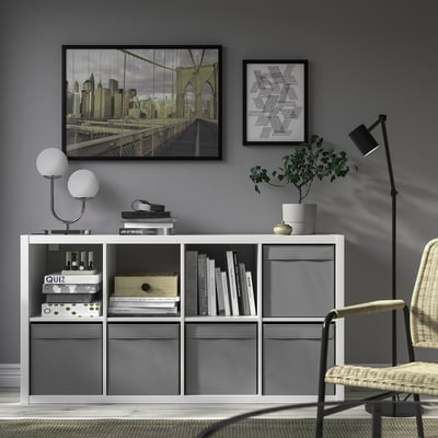 Modernt vardagsrum med tv, förråd, lampa, växt, konstverk och korgstol.