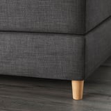 Närbild av en modern säng mörk stoppad hörn, med betoning på robust träben.