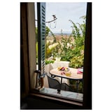 Fönstervy av en stol på en balkong med frukt och te, med utsikt över grönska och avlägset landskap.