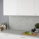 Modern köksbänk med vita skåp och bänkskiva i laminat med kalkstenseffekt som visar en skärbräda i trä, avokado och köksredskap.