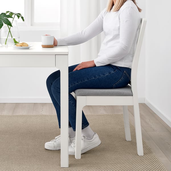 Person som sitter vid utdragbart vitt matbord med stoppad stol.