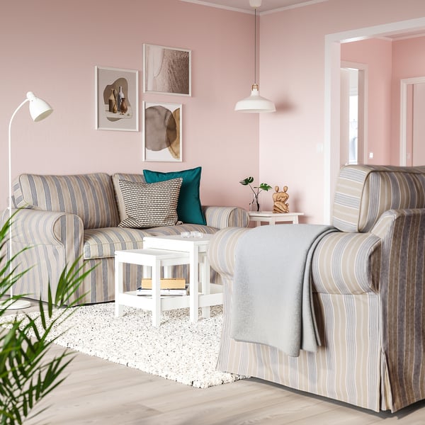 Ett mysigt vardagsrum, en grå- och vitrandig EKTORP-soffa med ett litet sidobord, växt och lampor i ett rum med rosa väggar.