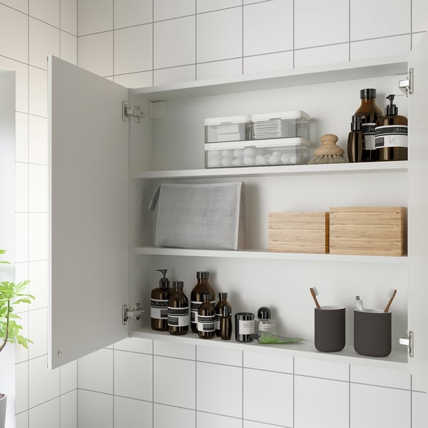 Öppet badrumsskåp med spegeldörrar som visar hyllor och innehåller olika föremål som toalettartiklar, behållare och trälådor.