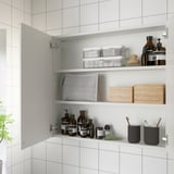 Öppet badrumsskåp med spegeldörrar som visar hyllor och innehåller olika föremål som toalettartiklar, behållare och trälådor.