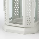 Vit metalllykta med intrikata blommiga utskärningar, designad för ljus.