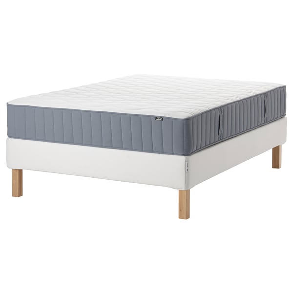 Blå och vit madrass på vit sängram med träben. IKEA-produkt.