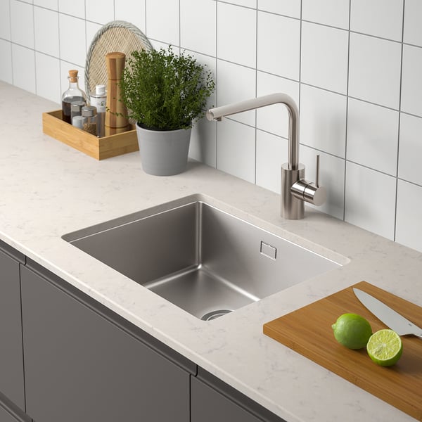 Modern diskbänk med kran i rostfritt stål, limefrukter, kniv på skärbräda och örter.