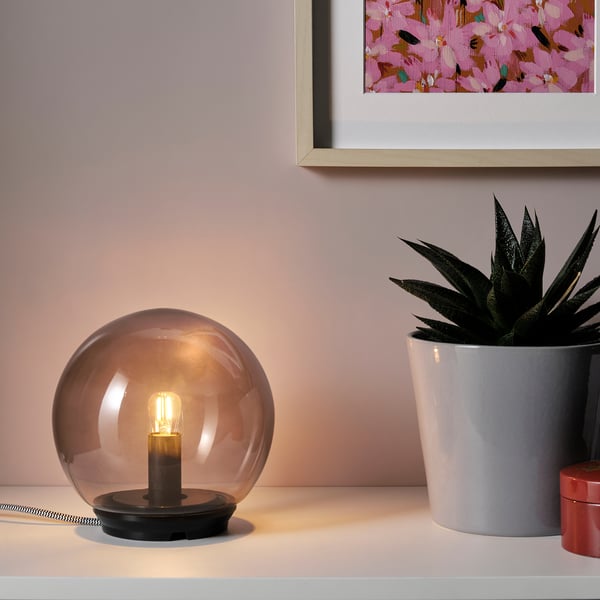 Modern grå klotlampa med svart bas och växt.