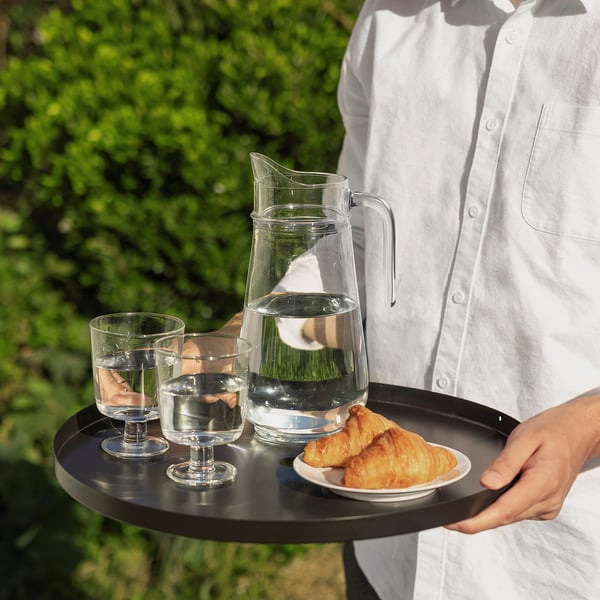 Person som håller bricka med kanna, två glas och bakverk; Servering utomhus.