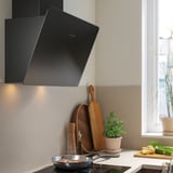 Modern svart köksfläkt, elegant design, glasyta, led-lampor, ovanför spishällen, nära fönstret.
