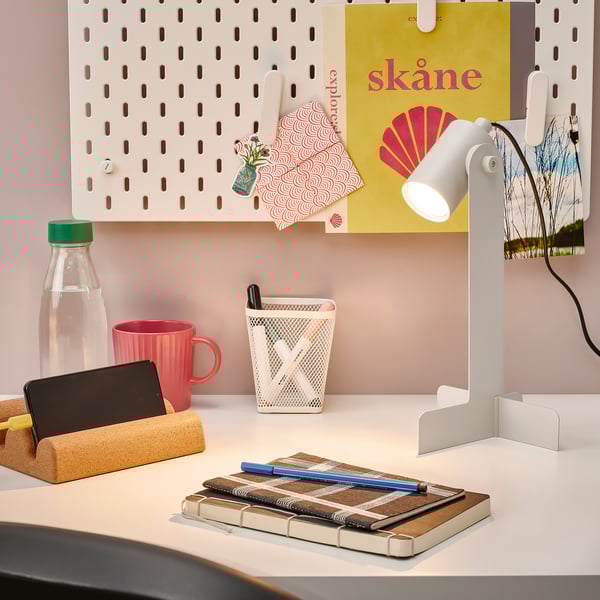 Skrivbord med FLOTTILJ-lampa, röd mugg och anteckningsbok. Elegant och effektiv.