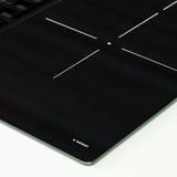 Svart induktionshäll med fyra brännare och touchkontroller. Varumärkesboost synlig i hörnet.