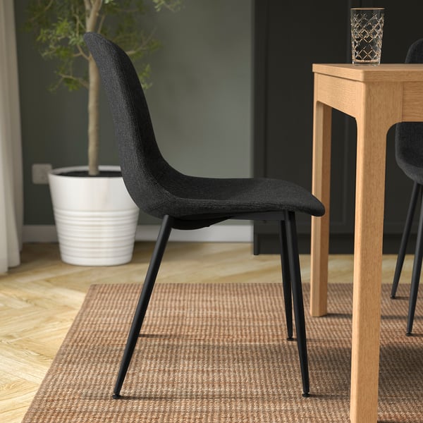 Svart GALLERUD stol nära ljust träbord, passar bra i rymden, med modern design och återvunnet material.