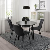 Modern matplats med 4 svarta stolar, runt bord, taklampa och en matta.