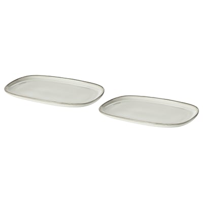 Två vita ovala GLADELIG-tallrikar i stengods. De har en enkel, elegant design med en sandig glasyrfinish.