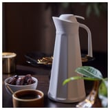 Vit termos med dadlar, kaffe och växt. Elegant, räfflad design.