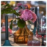En gul åttkantig glasvas med rosa blommor på ett träbord. Ingår i kollektionen GOKVÄLLÅ.