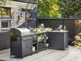 Modernt utekök: grill, bänk, diskbänk, färskvaror, växter, däck, elegant design.