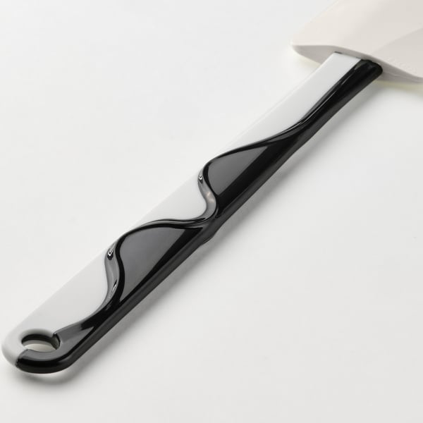 Svart och vit spatel med silikonblad, vilande på en vit yta. Designad för säker, repfri användning på non-stick-ytor.