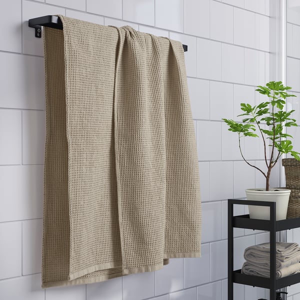 Handduk: GULLDYNA, beige, bomull, rektangulär, enkel. Hänger ovanför vikta handdukar och växt.