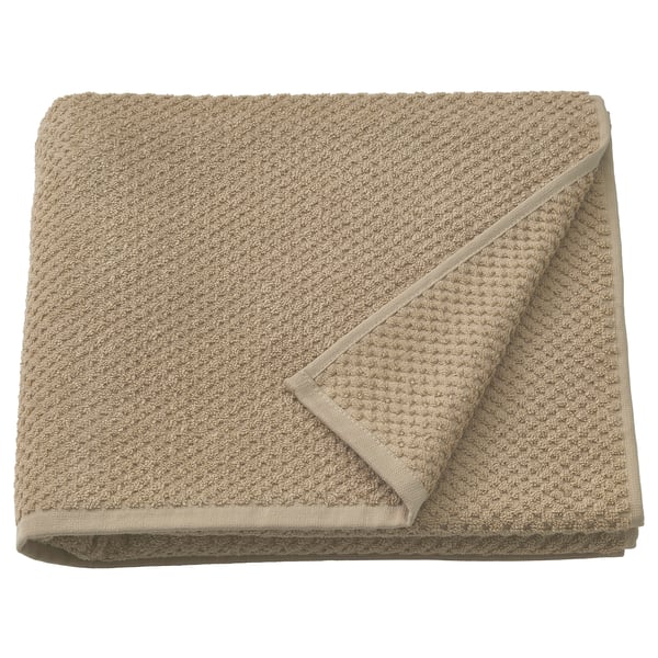 Den här bilden visar en beige GULVIAL-handduk, gjord av mjuk 100 % bomull, snyggt vikt. Dess tjocka, fluffiga konsistens är synlig.