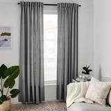 Grå gardiner hänger bredvid vit soffa med kuddar, filt, växter. Hög, draperad, återvunnen polyester.