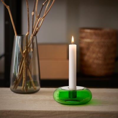 Liten grön ljusstake i återvunnet glas HÄNGBJÖRK med tänt ljus, bredvid hög vas med grenar.