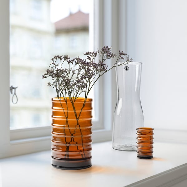 Tre vaser i brunt, klart och räfflat glas med torkade blommor på vit yta.