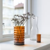 Tre vaser i brunt, klart och räfflat glas med torkade blommor på vit yta.