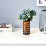 Liten bärnstensfärgad glas HÄNGBJÖRK vas med blå blommor på skrivbordet, bredvid trave med böcker och klar vas.