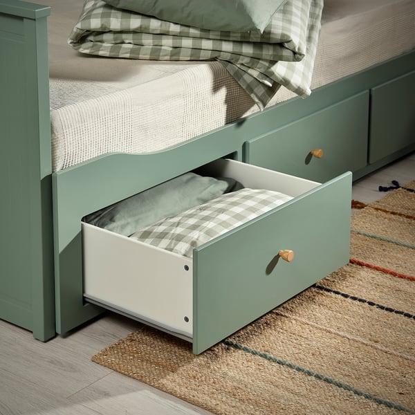 Den öppna lådan med den gröna dagbädden HEMNES avslöjar hopfällda sängkläder och visar förvaringsfunktionen.