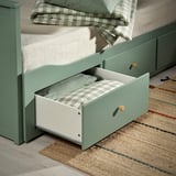 Den öppna lådan med den gröna dagbädden HEMNES avslöjar hopfällda sängkläder och visar förvaringsfunktionen.