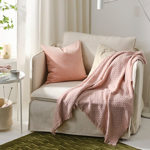 Beige HORNMAL fåtölj med ljusrosa pläd och kuddar i mysigt vardagsrum.