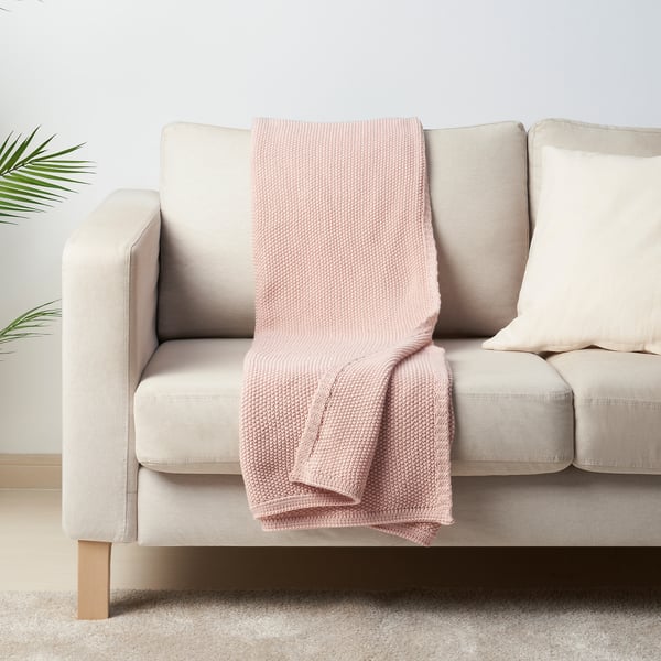 Ljusrosa HUMLEMOTT pläd på neutral soffa, mjuk, stickad, mysig, medelstor.