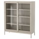Ett IDÅSEN-skåp i beige. Den har skjutdörrar i glas och fyra invändiga hyllor. Den moderna designen är robust med en metallram och härdat glas.