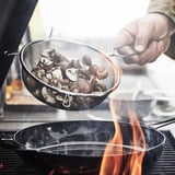 En person håller en nätsil med svampar över en kastrull med lågor.