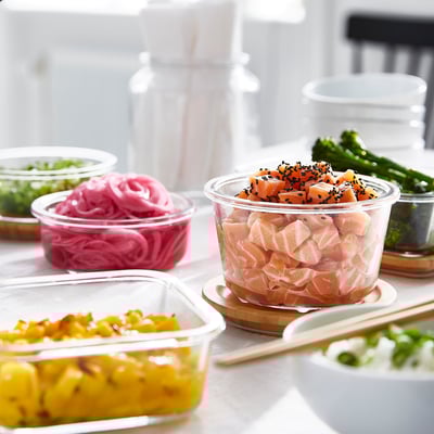 Olika glasbehållare med lock fyllda med olika livsmedel, inklusive lax och grönsaker, arrangerade snyggt på ett bord.