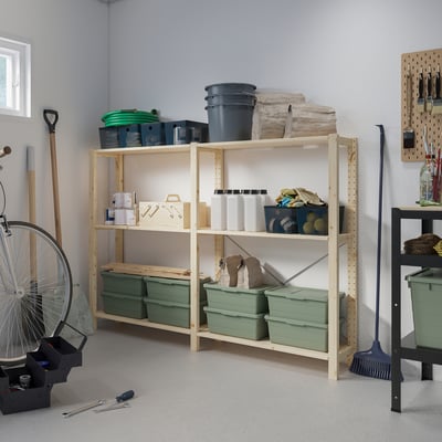 Stora ljusa IVAR trähyllor med gröna plastkärl i garaget, omgivna av olika verktyg och utrustning.